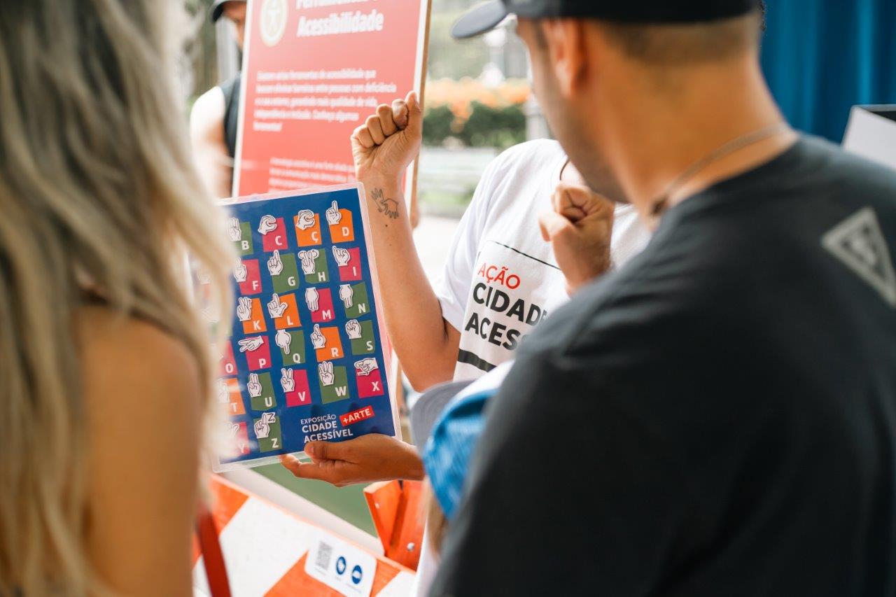 Duas pessoas observam uma tabela de mão do alfabeto em Libras,