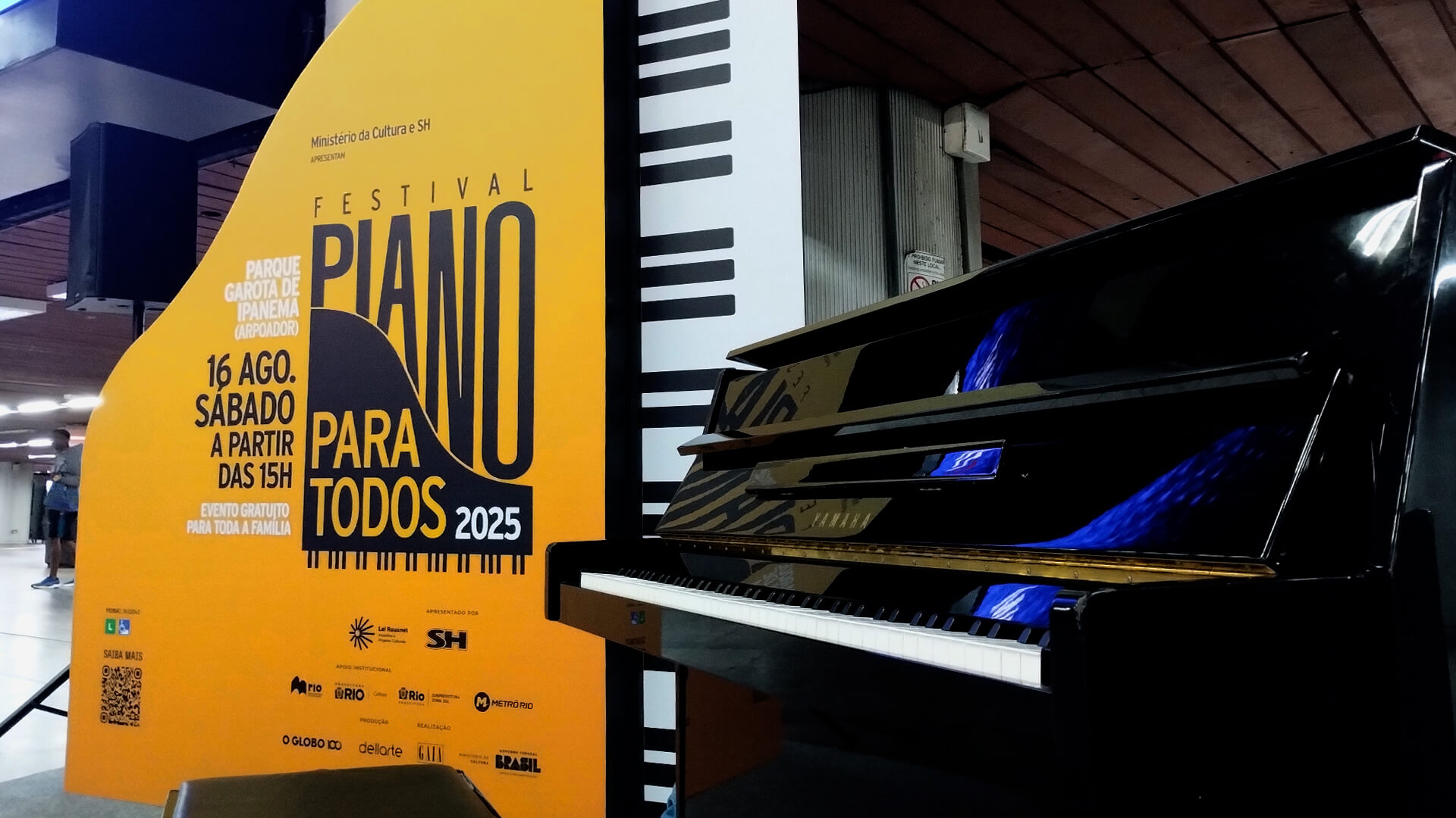 Piano preto,  e um painel com formato de piano, com fundo degrade do laranja para o amarelo e com informações sobre o evento.