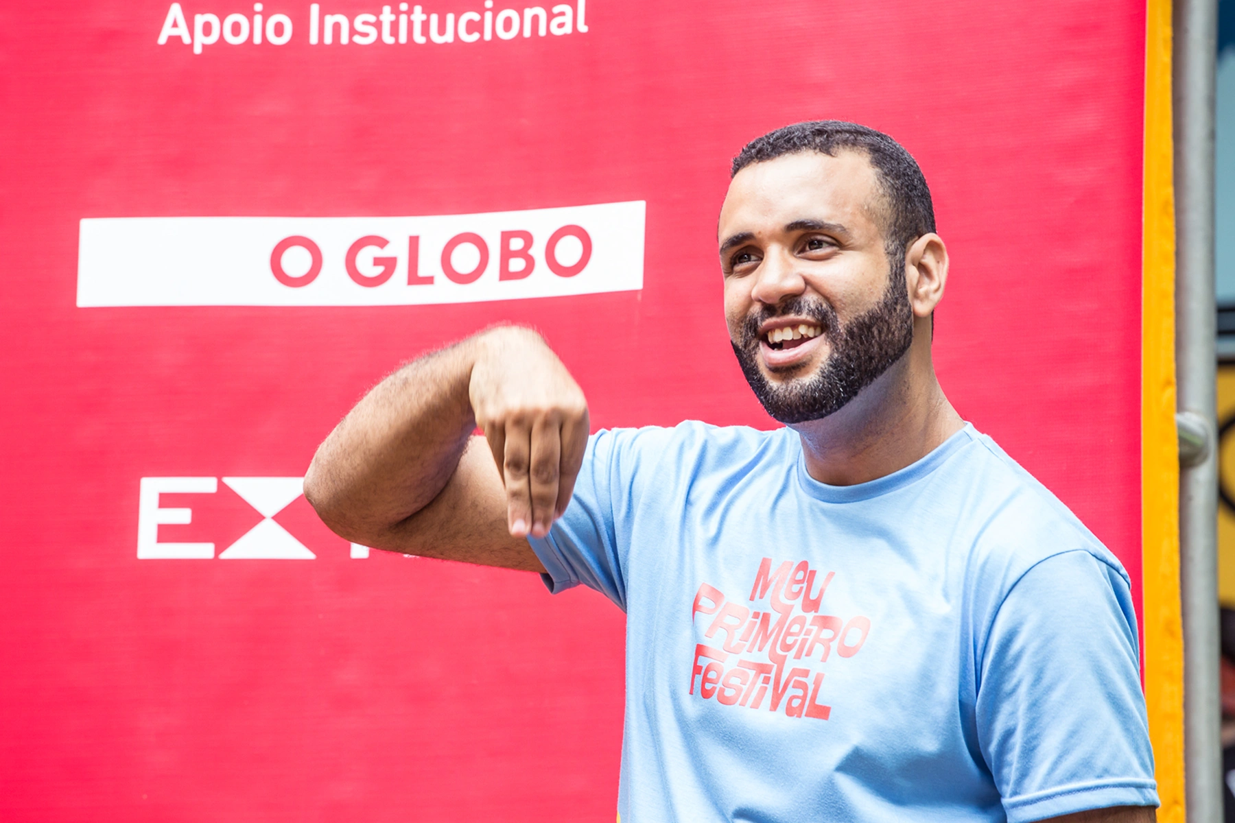 Interprete de Libras gesticulando com a mão direita, ele feste uma camisa azul com a marca do 
