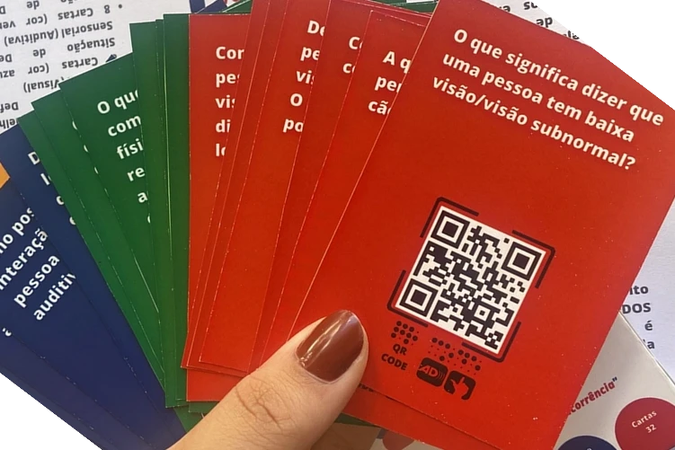 Cartas coloridas de um jogo sobre acessibilidade, elas possuem fundos nas cores vermelho, verde e azul, texto escrito em branco e um grande Qrcode.